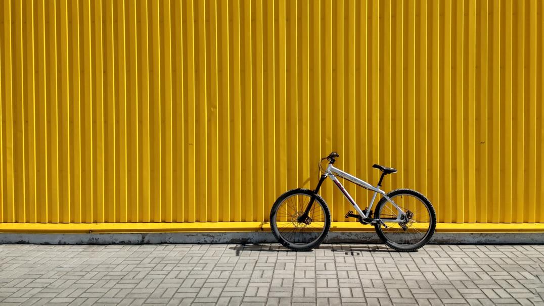 A bike propped up a yellow wall waiting for the owner, a transfer student, to come back and ride away into a new future