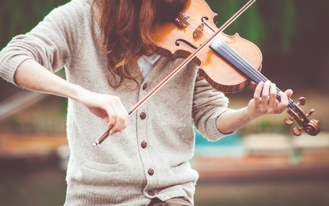 A young girl with brown hair in a grey sweater playing the violin